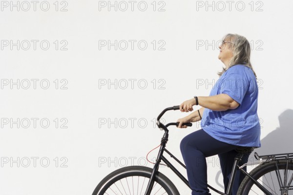Smiling overweight mature woman riding a retro style bicycle isolated on white background and copy