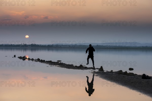 Unrecognised person running to reach the sun. Idyllic winter sunset at a lake. Silhouette