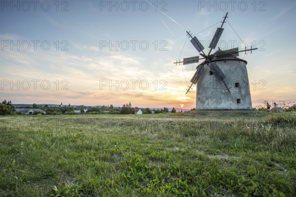 Windmill with wooden sails in a landscape with fields. Meadows and flowers appear in the sunset.