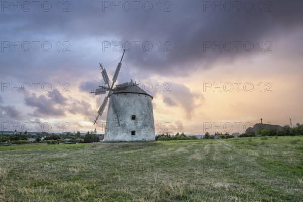 Windmill with wooden sails in a landscape with fields. Meadows and flowers appear in the sunset.