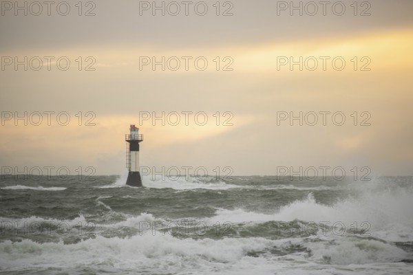 A lighthouse stands in the storm. Wild sea in the evening. Sunset on a coast with many rocks in the