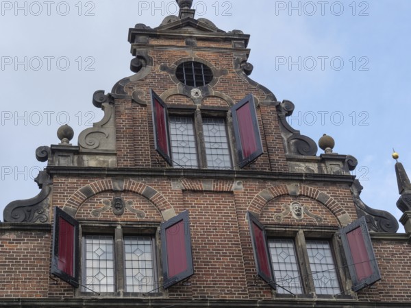 Historic brick façade with decorative elements and red shutters against a cloudy sky, nijmegen, the