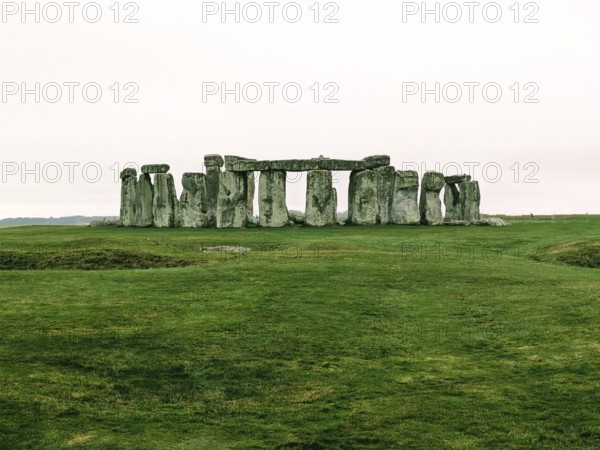 Warm-toned image of Stonehenge on a grassy field under a cloudy sky. Salisbury, England, United