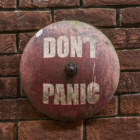 Isolated Rustic Vintage Red Alarm Bell With The Words Don't Panic In White Against A Red Brick Wall