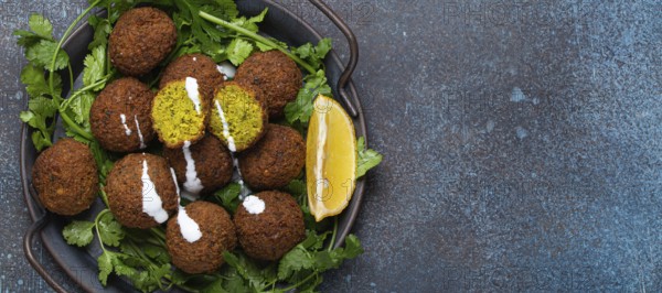 Plate of fried falafel balls served with fresh green cilantro and lemon top view on rustic concrete