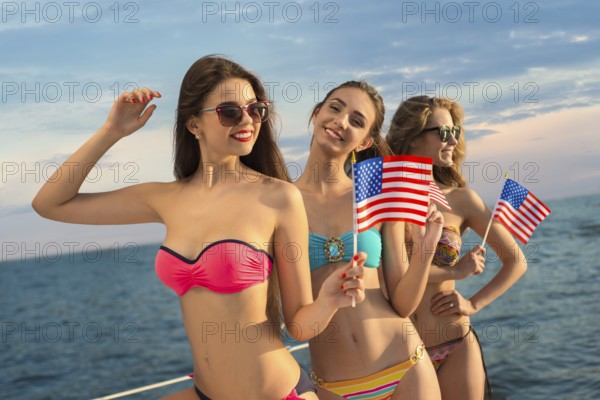 Girls resting on the sea. American girls. Girls patriotic with American flags. Girls waving the