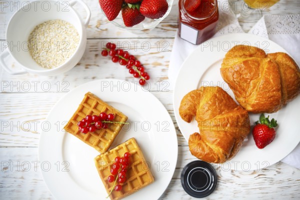 Waffles with red currant jam and berries on a white plate, croissants, orange juice and oat flakes