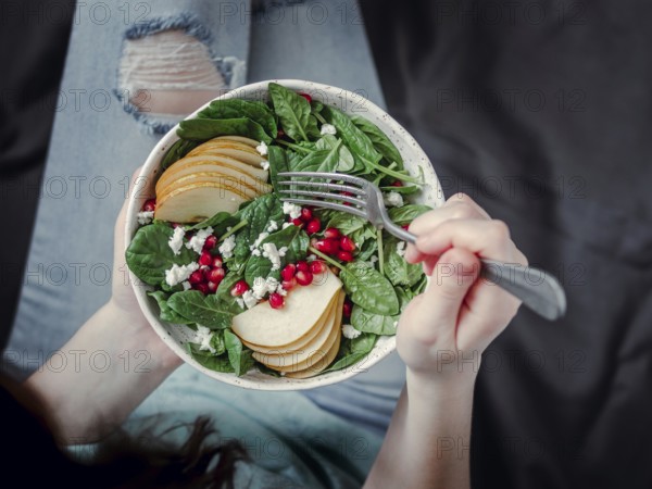 Woman in jeans holding vegan salad bowl with spinach, pear, pomegranate, cheese. Vegan breakfast,