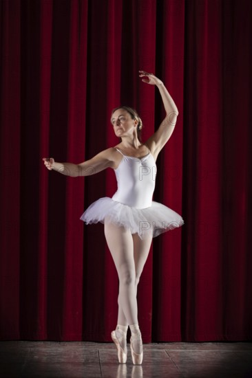 Ballet dancer in white ballet tutu in front of a red stage curtain in elegant pose, Mindelheim City