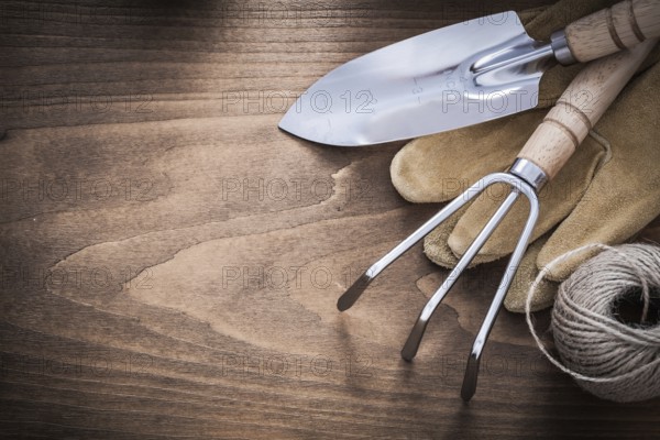 Metal hand spade rake brown leather gardening gloves and hank of string on vintage wood board