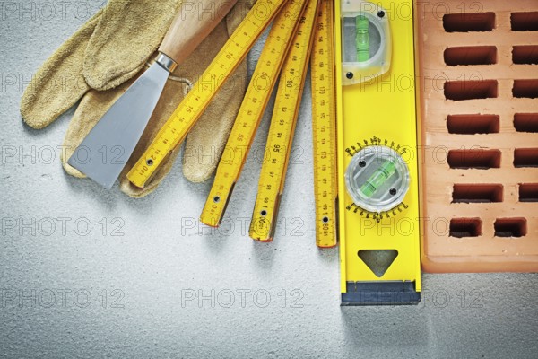 Red brick protective gloves putty knife construction level wooden meter on concrete background