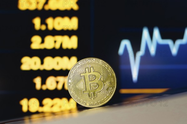 In this photo illustration, a Bitcoin coin is seen on the table and in the background, a stock
