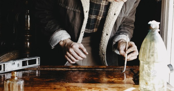 A person concentrated on applying varnish on wood with a bottle nearby