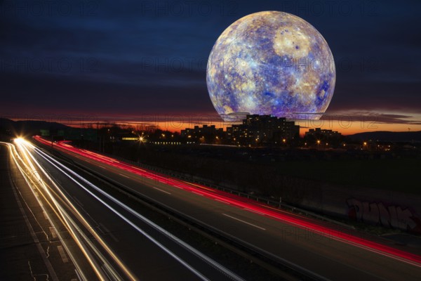 Surreal night sky with a huge moon over a town and traces of light from cars on the motorway at