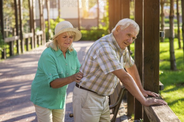 Senior male leans on fence. Elderly couple outdoors. Pains in lower back. Old traumas influence