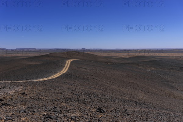 A view of a dirt road leading through the rock and sand desert of southeastern Morocco mear