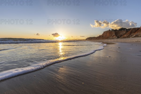 Beautiful sandy beach with red rocks and cliffs. Twilight at sunset with shallow waves on the