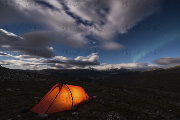 Northern Lights (Aurora borealis) over illuminated tent, Rapadalen, Sarek National Park, Laponia