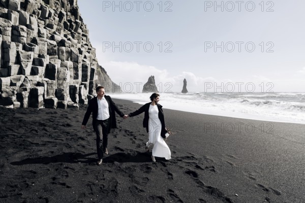 Destination Iceland wedding. A wedding couple walks along the sandy black beach of Vik, near the