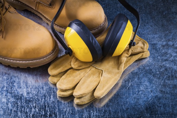 Leather safety boots gloves and noise insulation ear muffs on scratched metallic background