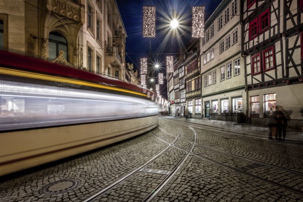 Langzeitbelichtung einer Straßenbahn, die durch eine historische Straße mit Fachwerkhäusern fährt,