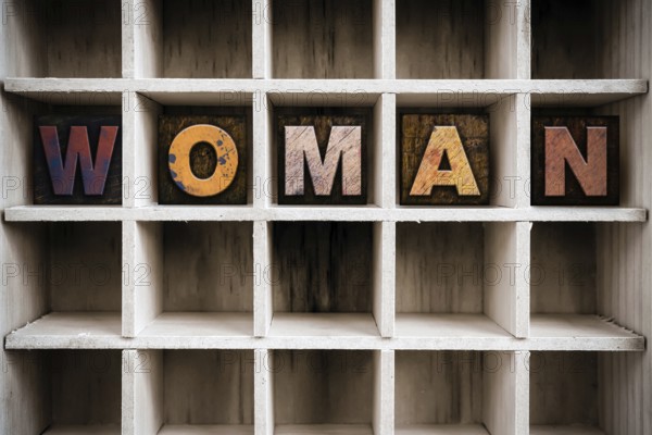 The word WOMAN written in vintage ink stained wooden letterpress type in a partitioned printer's
