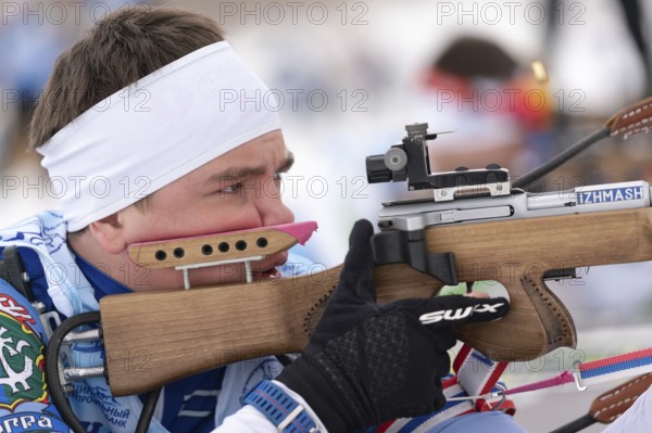 Close-up view of sportsman biathlete aims rifle shooting prone position. Biathlete Andrey Krutov in