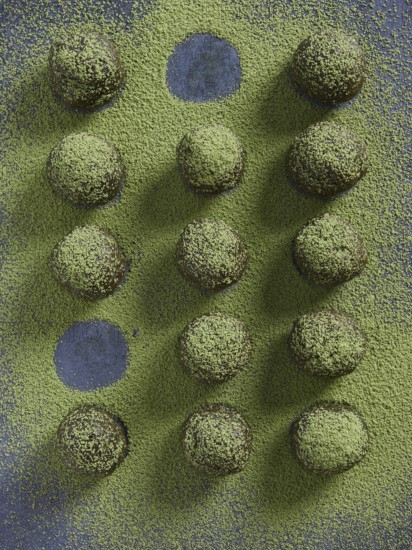 Bliss balls or energy balls sprinkled with matcha green tea. Placed in a row with some round holes