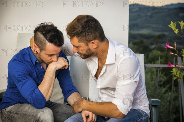 Portrait of two handsome men having trouble in relationship while sitting hugging and sad on
