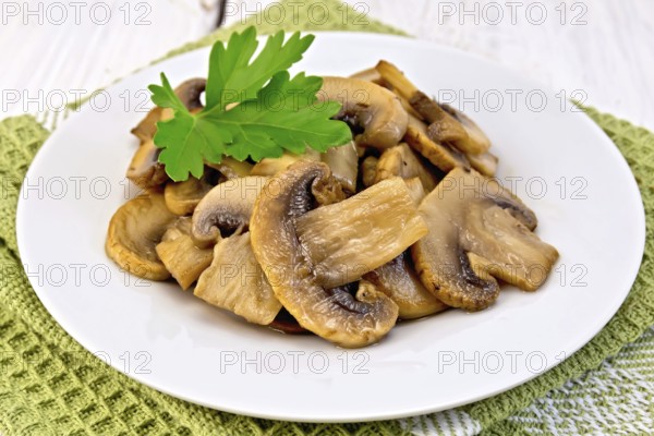 Champignons fried in a plate with a leaf of parsley on a napkin on the background light wooden