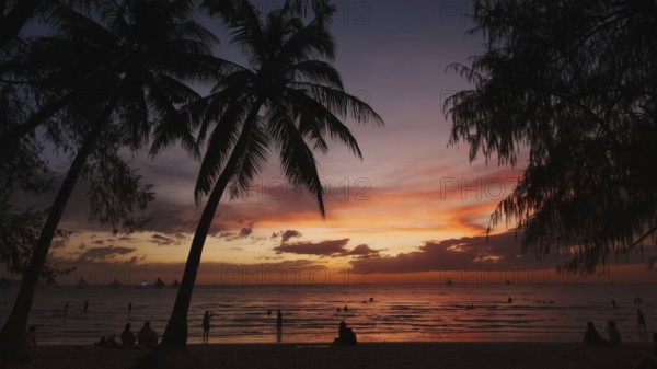 Silhouetted people and palms near sea. Sunset at tropical White beach, Boracay island, Philippines,