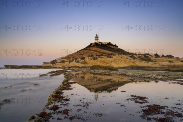 A view of the Cabo de la Huerta lighthouse at sunrise with reflections in tidal pools in the
