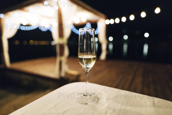A glass of champagne stands on the table against the backdrop of a party on the beach. Beach talk