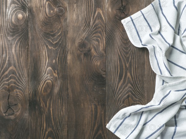 View from above on brown wooden table with linen kitchen towel or textile napkin. Blue tablecloth