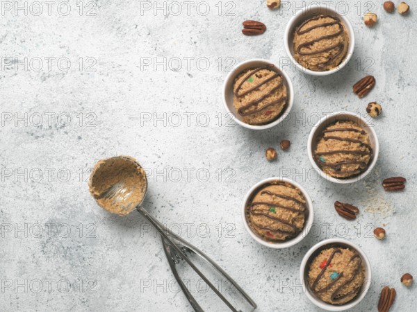 Safe-to-eat raw monster cookie dough in small portion bowl, ice cream scoop and nuts on gray cement