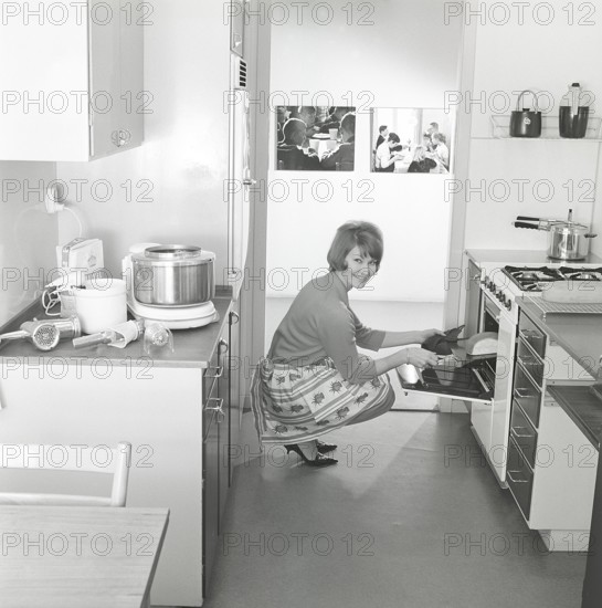 In the kitchen in the 1960s. A young woman in the kitchen taking out the ready baked breads from