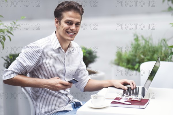 Smart attitude. Positive handsome man using a laptop and sitting in the cafe while surfing the
