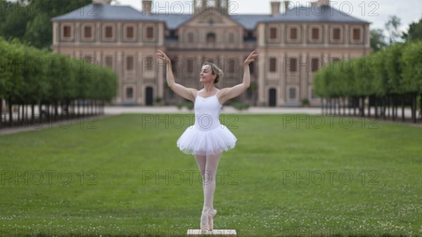 Ballerina in a white tutu dancing in the park of a palace, surrounded by green trees and