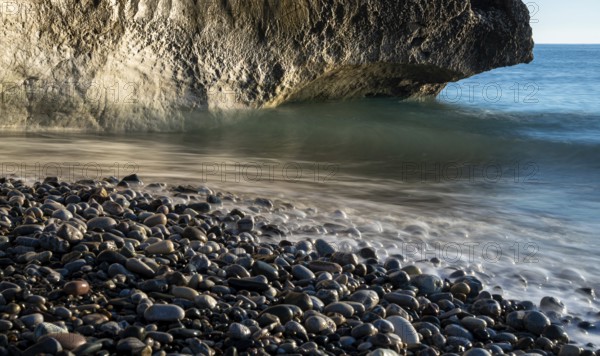 Low angle view of seascape with windy waves splashing on the rock and the sea pebbles. Rock of