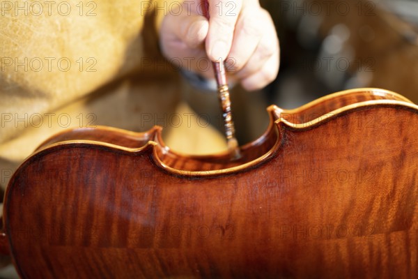 Luthier carefully varnishing a violin with a brush, showcasing the craftsmanship and meticulous