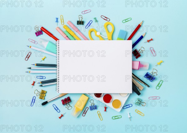Notebook with stationary objects on blue background. Empty white paper sheet of notepad or