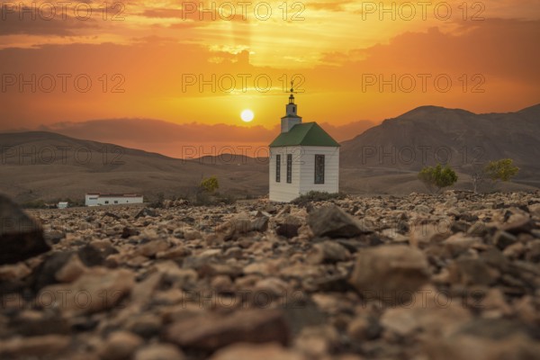 Small, sweet white wooden chapel in a barren volcanic landscape. Sunset, landscape shot of the