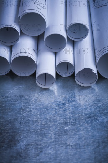 Pile of rolled engineering drawings on scratched silver-metal background building and architecture