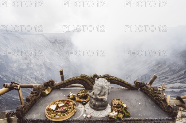 Traditional offerings and a statue on an altar with a misty volcano background, Bromo volcano, Sri
