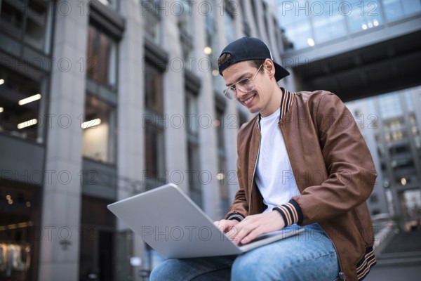 Happy handsome student looking at computer screen while typing something on laptop keyboard during