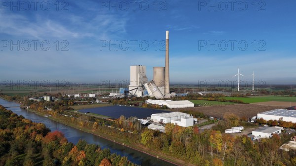 Industrial landscape with power plant and wind turbines, surrounded by autumn trees along a canal,