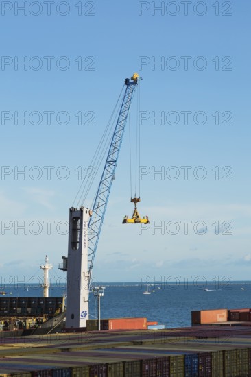Gotwald crane with lifting attachment and stacked rectangular metal box shipping conatiners on dock