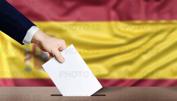 Hand holding ballot in the ballot box with the flag of Spain in the background. Spain general