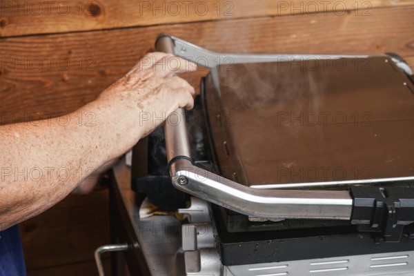Senior hand closing metal electric grill, smoke coming up from grilled food inside, Pribylina,