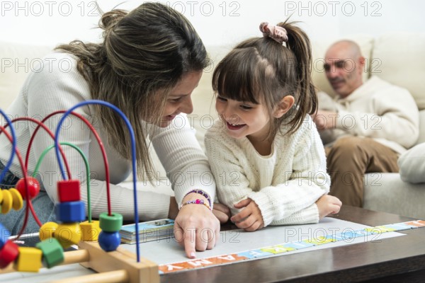 Happy family playing with alphabet puzzle, mother teaching daughter letters, father watching them,